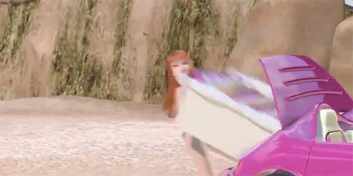 A GIF of Midge, a Barbie character with red hair and a green bathing suit, pulling a white bookcase filled with pink books out of the trunk of a pink car.