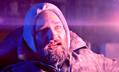 A gif of a white man with a frozen beard looking in fear at something off screen. Smoke from a flare can be seen at the right of the frame.